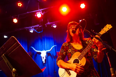 Performer singing and playing a bass guitar under red stage lights at the 2025 Jason Molina MusiCares benefit.