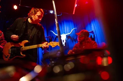 Electric guitarist and seated pedal steel player on stage at the 2025 Jason Molina MusiCares benefit.