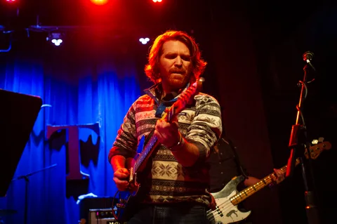 Singer holding a microphone with a bass guitar at the 2025 Jason Molina MusiCares benefit.