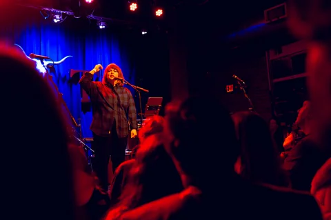 Vocalist performing under red and blue stage lights at the 2025 Jason Molina MusiCares benefit.