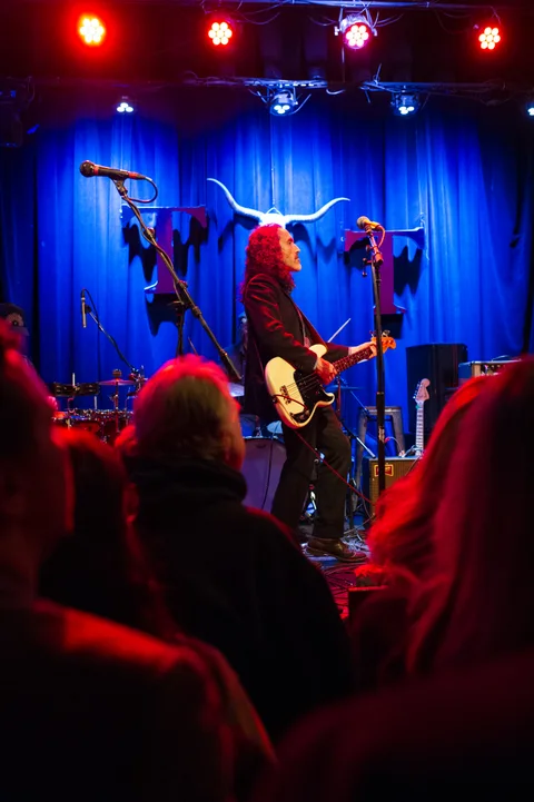 Guitarist in front of the blue stage curtain at the 2025 Jason Molina MusiCares benefit.