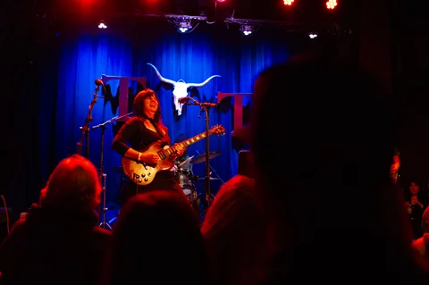 Electric guitarist in front of the blue stage curtain at the 2025 Jason Molina MusiCares benefit.