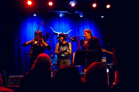 Three vocalists performing together at microphones at the 2025 Jason Molina MusiCares benefit.