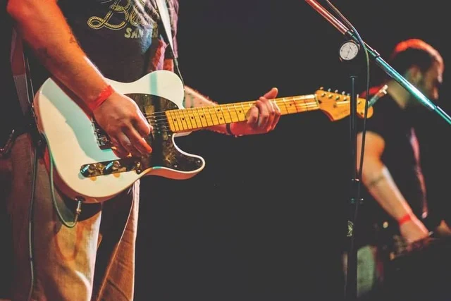 Close-up of a cream electric guitar and its player. The Trouble Starts, East release show, August 16, 2013.