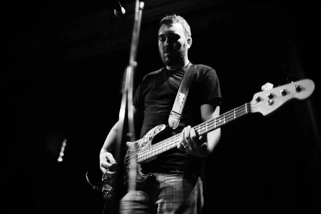 Black-and-white view of a bassist playing at a microphone. The Trouble Starts, East release show, August 16, 2013.