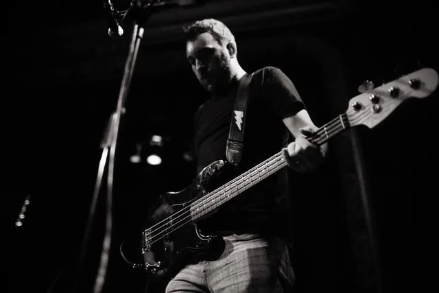 Black-and-white low-angle view of a bassist playing. The Trouble Starts, East release show, August 16, 2013.