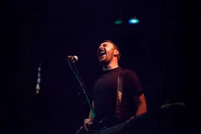 Bassist singing into a microphone on a dark stage. The Trouble Starts, East release show, August 16, 2013.