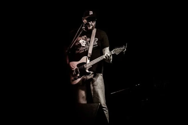Black-and-white view of a guitarist on a dark stage. The Trouble Starts, East release show, August 16, 2013.