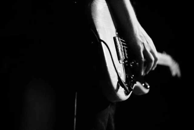 Black-and-white close-up of a hand on an electric guitar. The Trouble Starts, East release show, August 16, 2013.