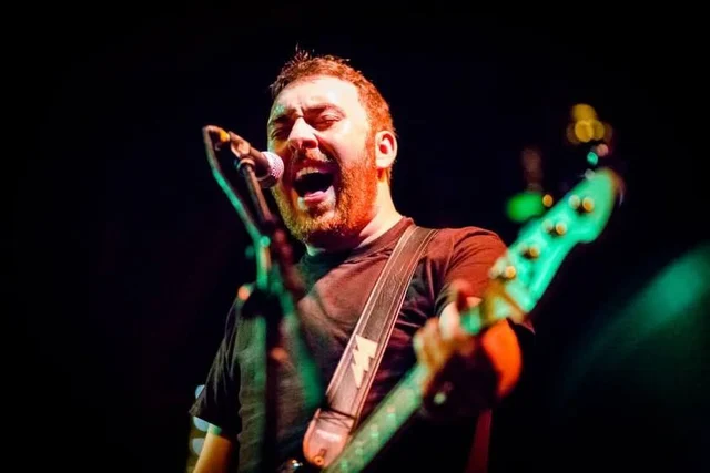 Bassist singing into a microphone under colored stage lights. The Trouble Starts, East release show, August 16, 2013.
