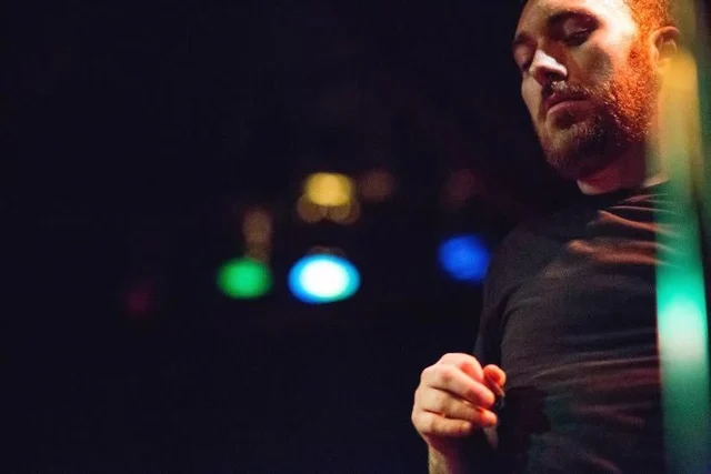 Close-up of a performer beside colored stage lights. The Trouble Starts, East release show, August 16, 2013.